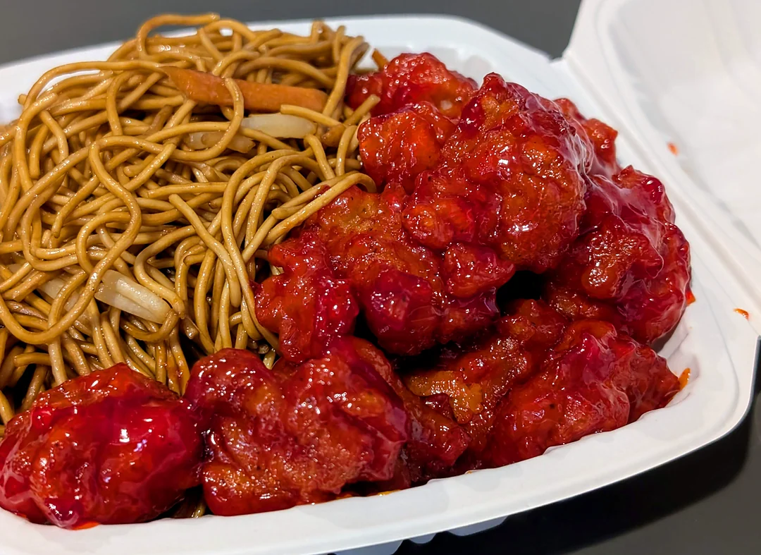 Sweet and sour pork with fried noodles in a takeout box